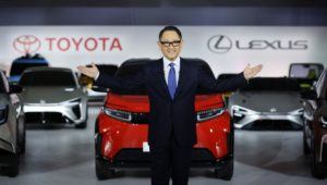 Akio Toyoda standing in front of Toyota and Lexus SUVs.